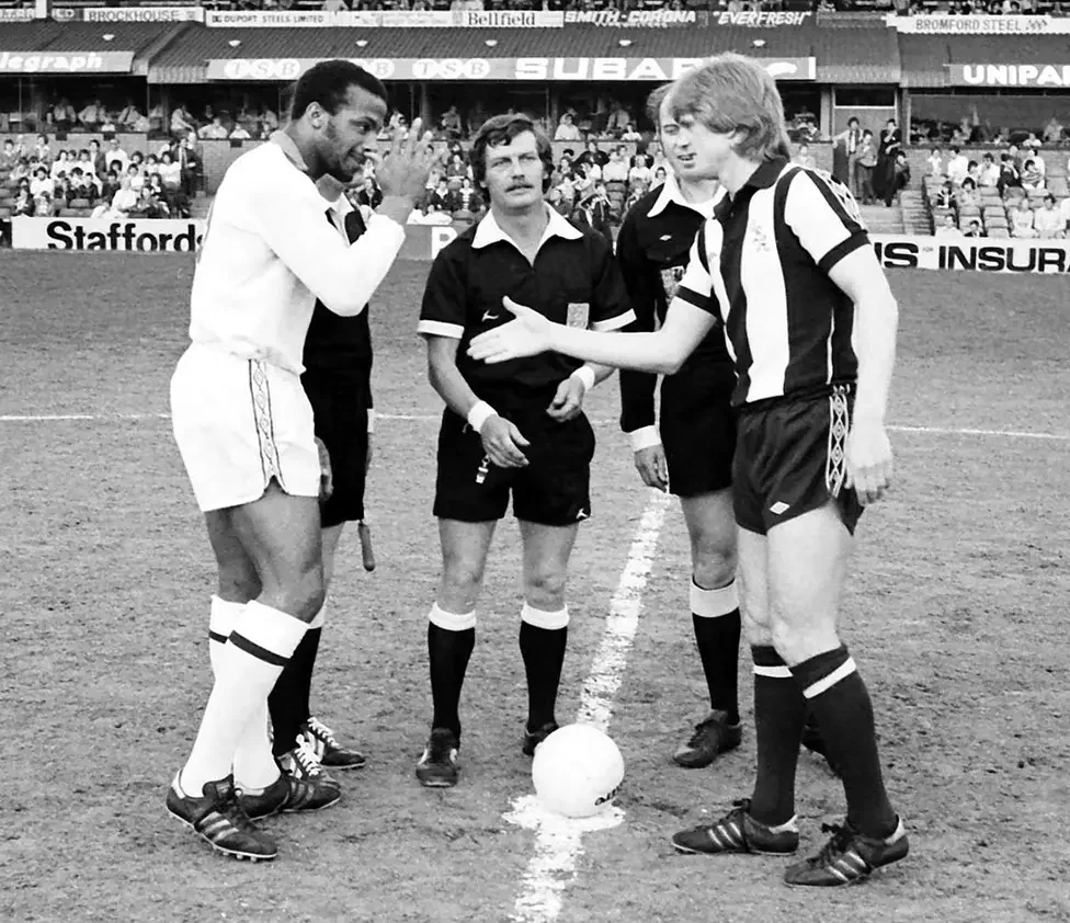 Two captains shaking hands at the centre circle before a match as the referee and linesmen look on