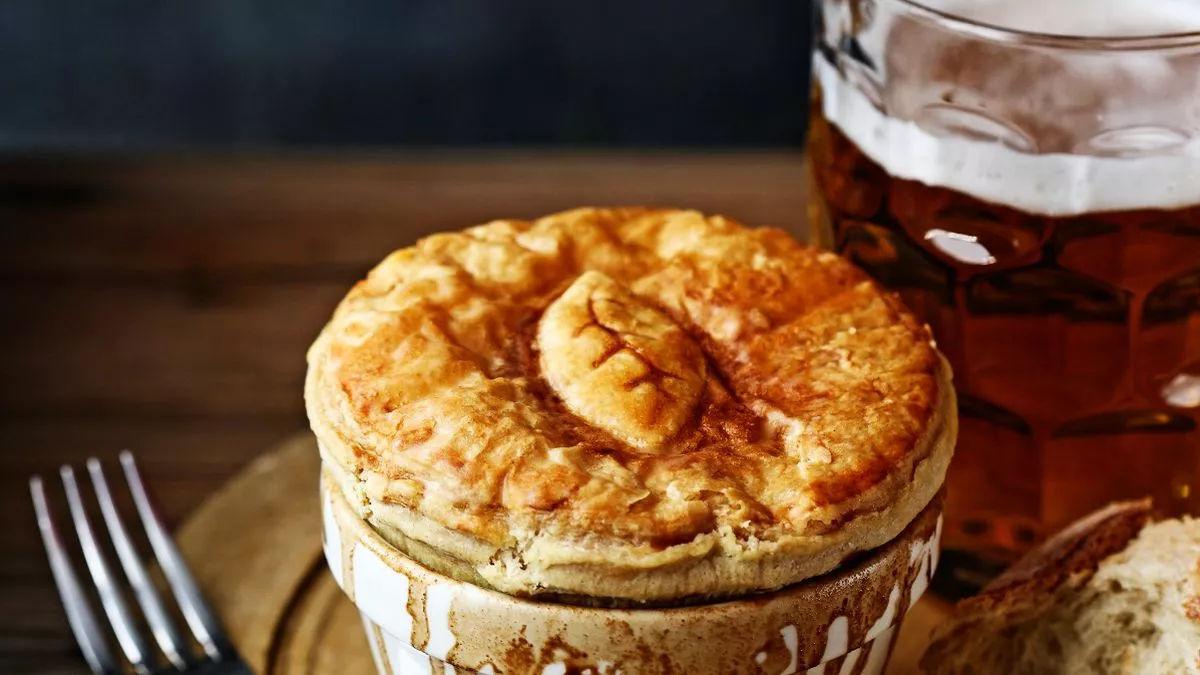 A golden-crusted pie in a ceramic dish beside a pint of beer