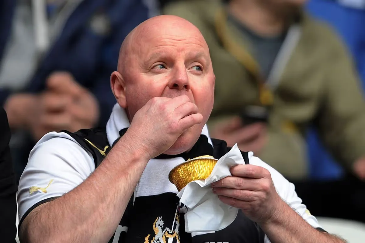 A football supporter in a scarf eating a pie in the stands